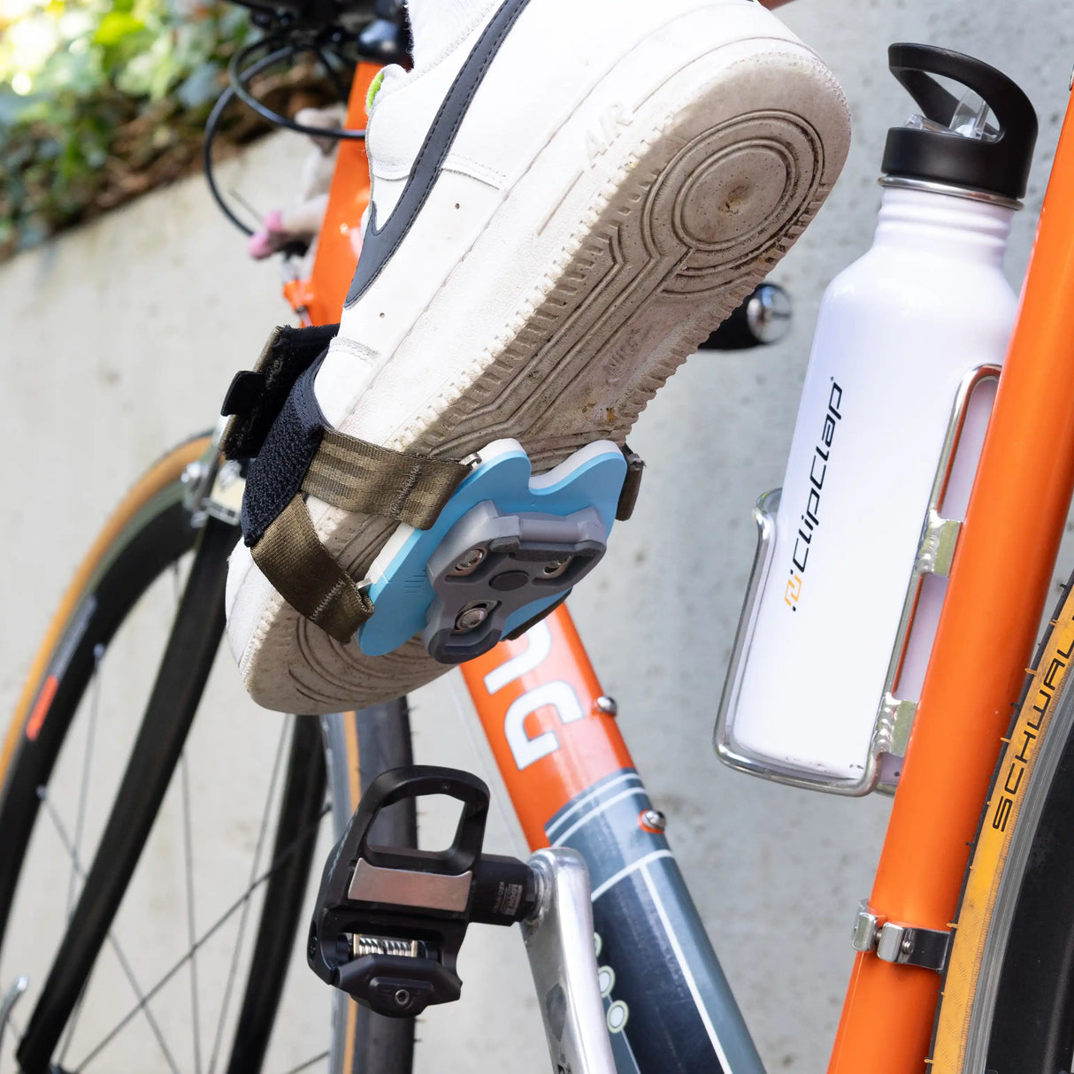 Weißer Sneaker klickt in Klickpedal ein durch Klickpedal-Adapter in oliv und blauer Grundplatte mit 2-Loch-Cleats am Schuh